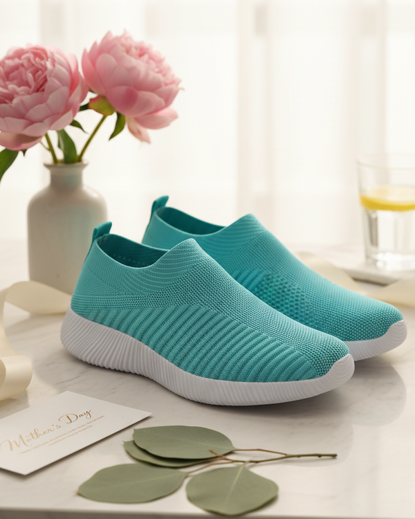 Turquoise slip-on shoes on a white surface with pink flowers in the background